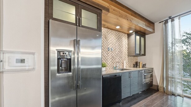 Una cocina moderna con un refrigerador de acero inoxidable, un lavavajillas y un salpicadero con motivo de espiga.