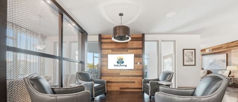 Una moderna zona de recepción con un logotipo, sillones de cuero, un panel de madera y un ventanal grande.