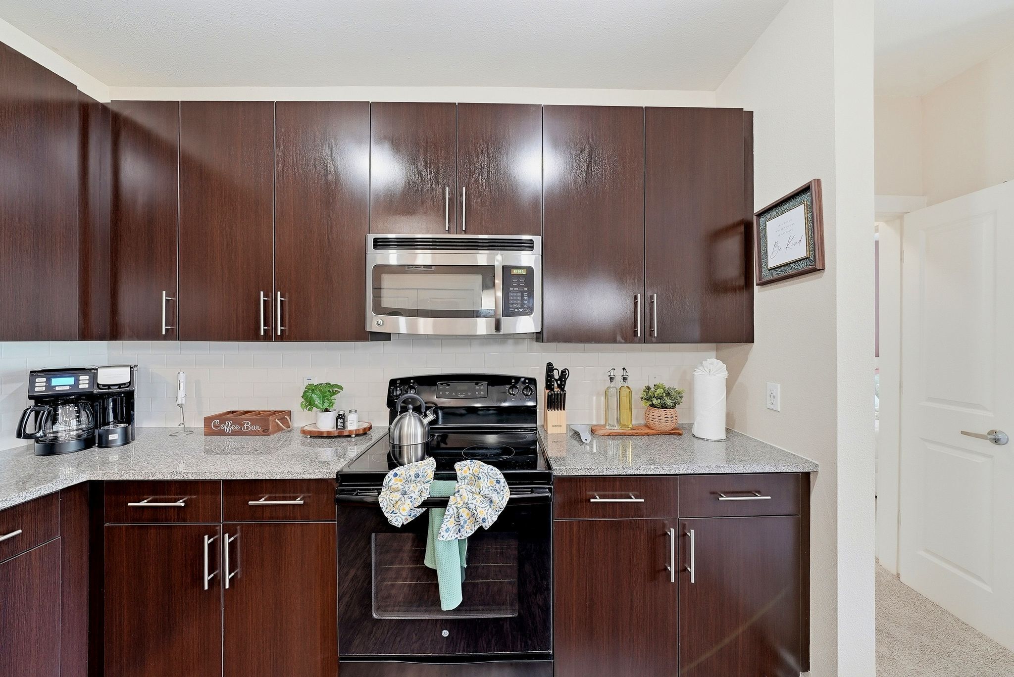 A kitchen with dark wooden cabinets, a stainless steel microwave, a black stove, and a coffee maker.