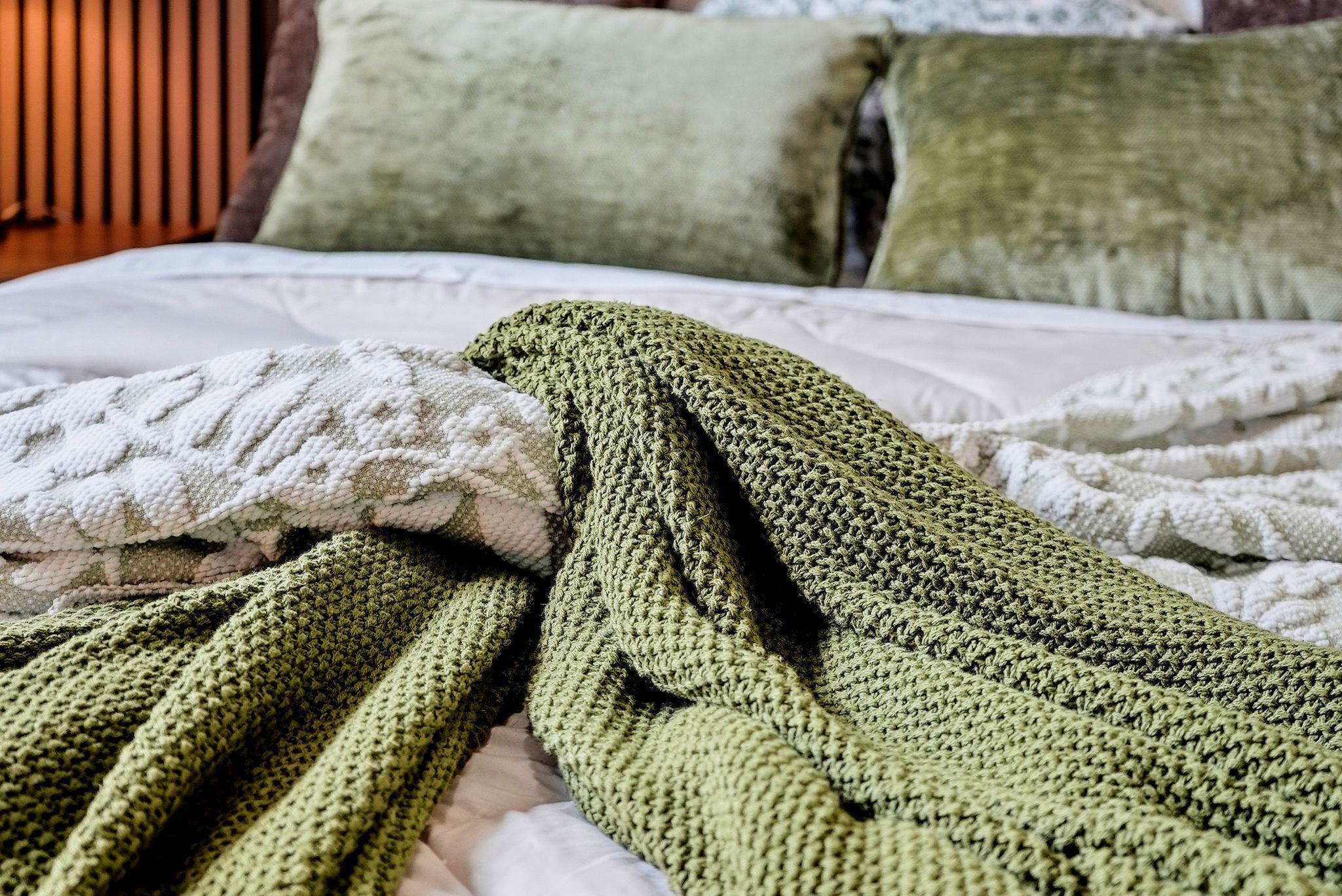 Un lit avec une couverture tricotée verte et un jeté tricoté blanc.