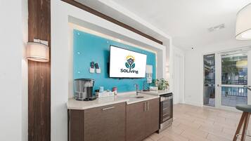 A modern kitchen with a blue backsplash, a coffee bar sign, and a mounted TV displaying the 'SOLiving' logo.