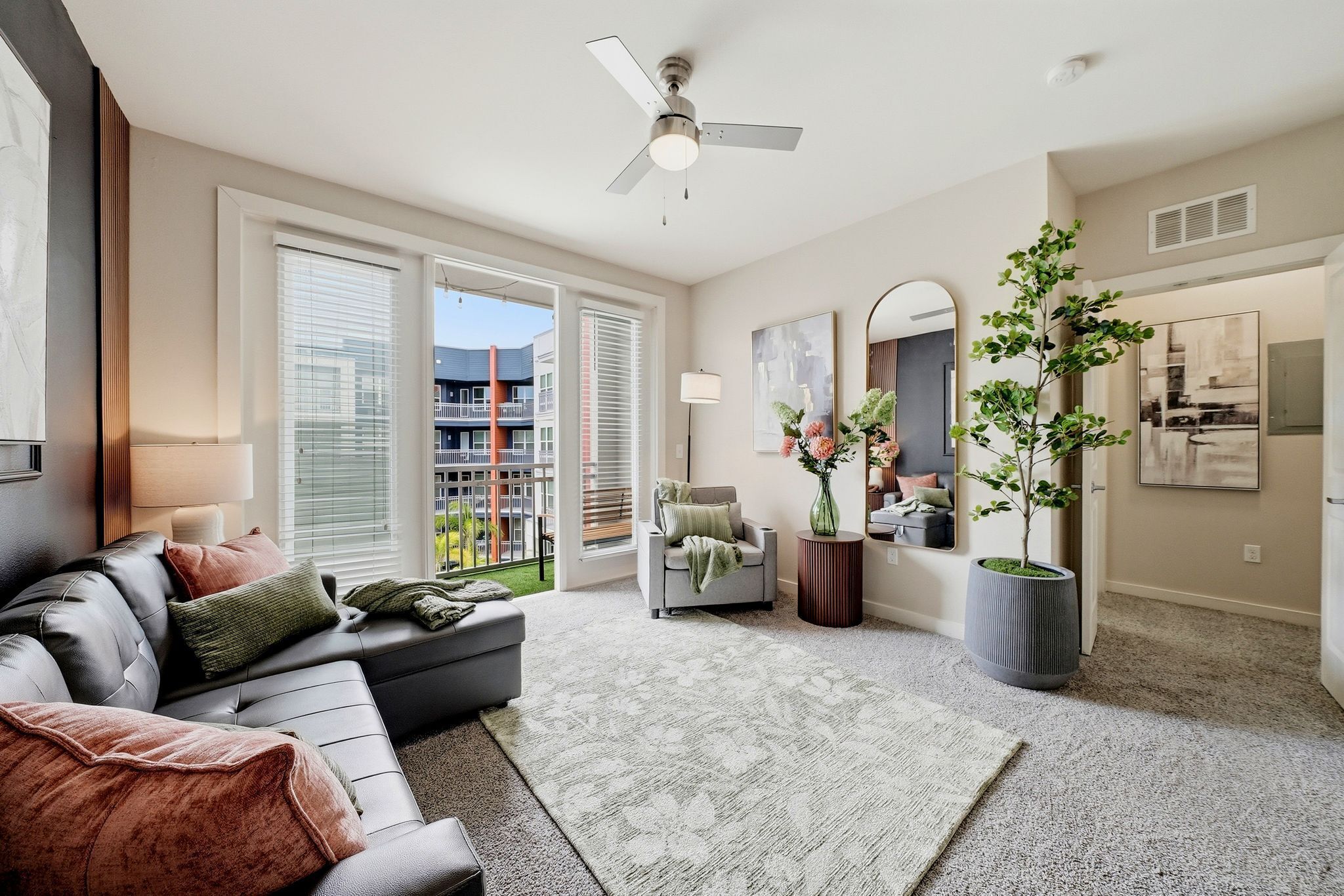 A living room with a sofa, a chair, a potted plant, a ceiling fan, and a large window.