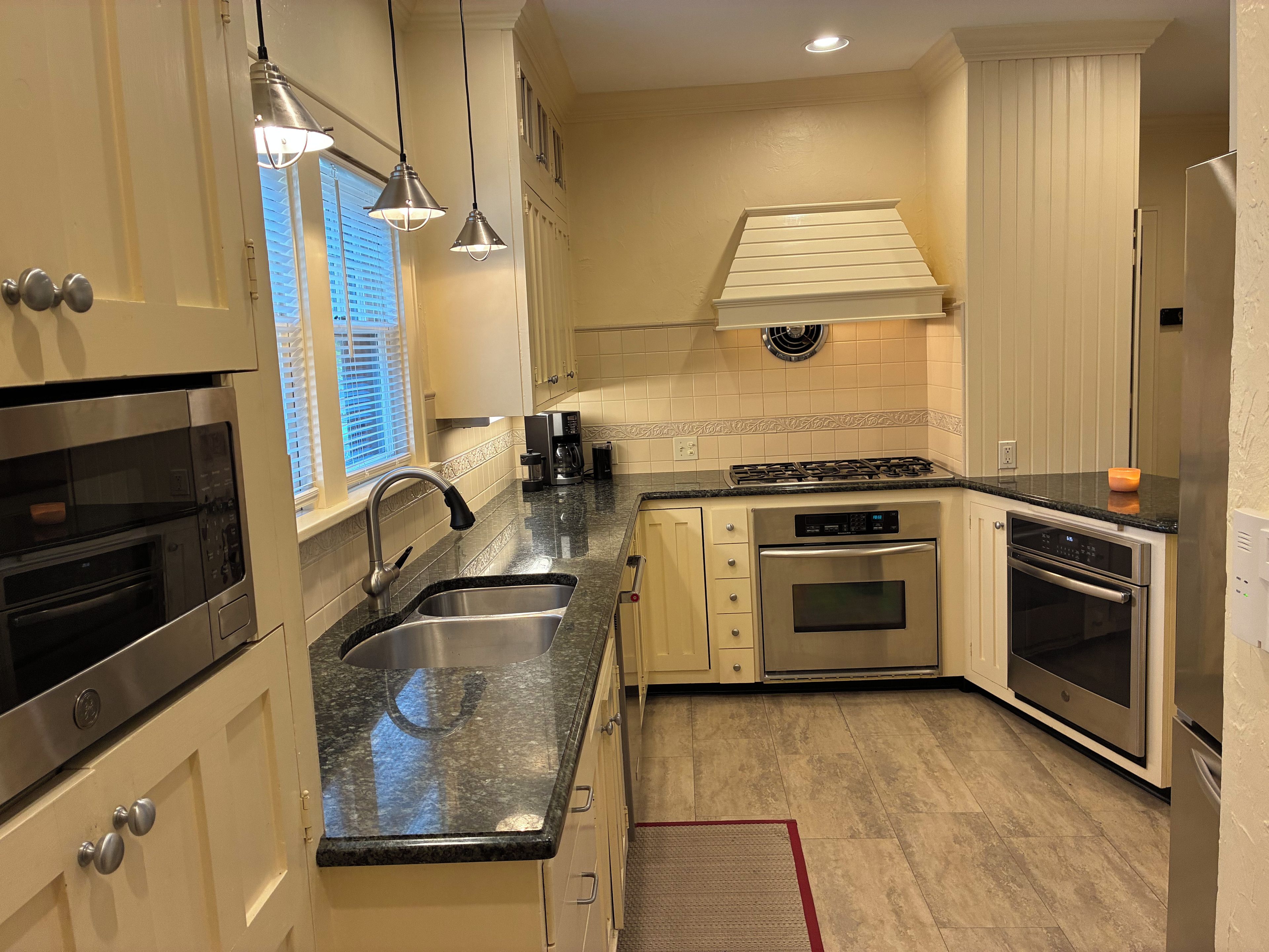 A modern kitchen with stainless steel appliances, a granite countertop, and a window with blinds.