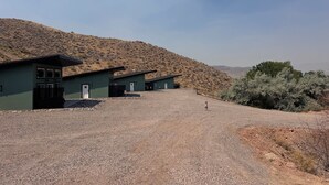 A building with a green exterior, a gravel driveway, and a hilly landscape in the background.