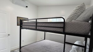 A bunk bed with a headboard, a door, a window with blinds, and a small rug.