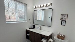A bathroom with a vanity, mirror, lights, toilet, and a rug.