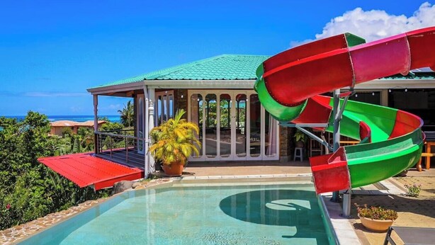 A pool with a water slide, a covered seating area, and a view of the ocean.