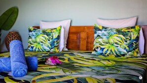 A bed with a tropical leaf pattern bedspread, two pillows with a similar design, and a blue towel on the bed.