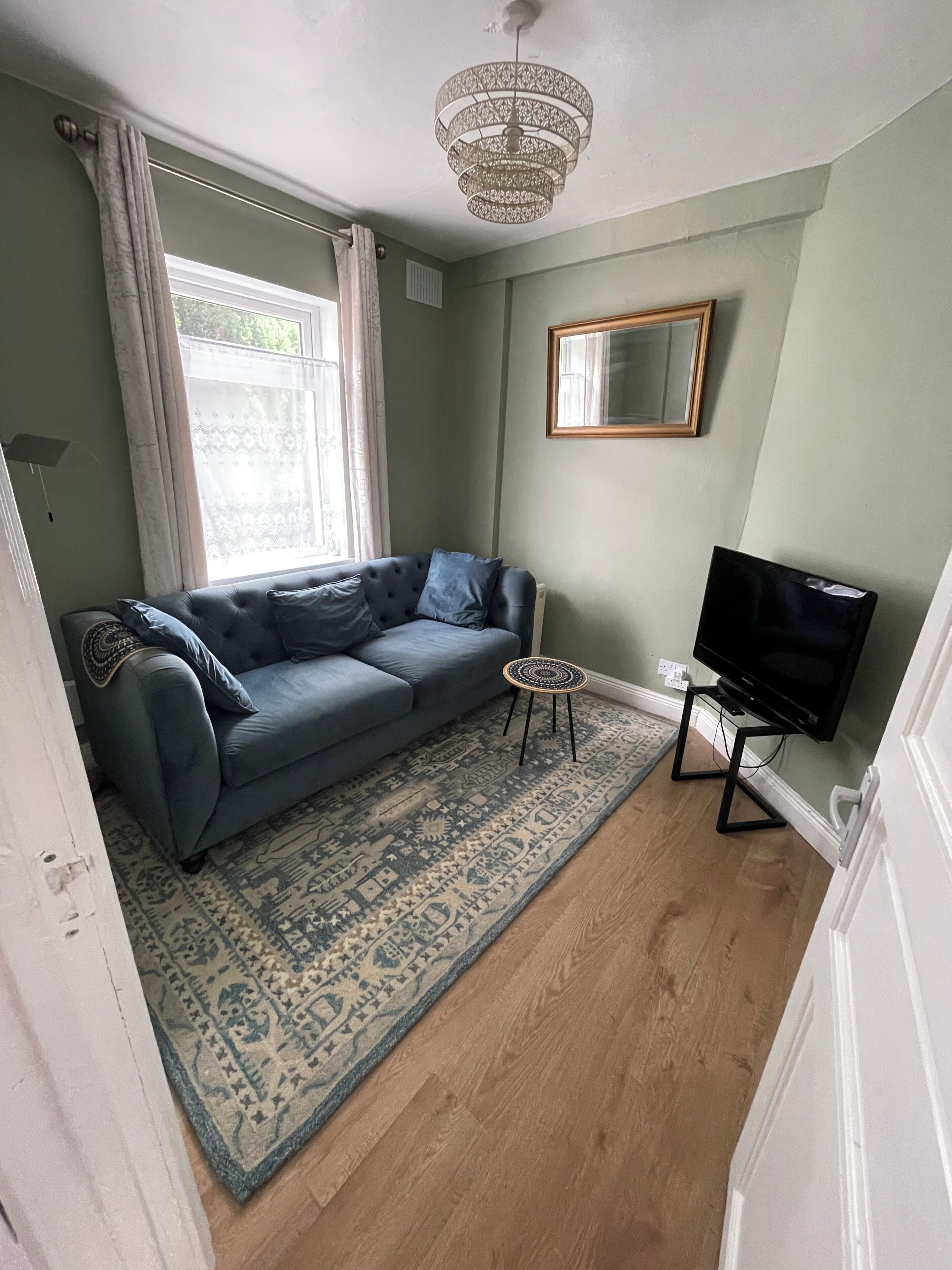 A living room with a blue sofa, a patterned rug, a television on a stand, and a ceiling light fixture.