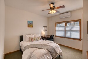 Une chambre à coucher comprenant un lit, un bureau, une chaise, un ventilateur de plafond et une fenêtre avec des stores.