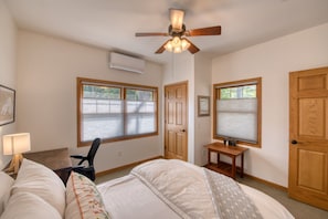 A bedroom with a bed, a desk, a chair, a ceiling fan, and two windows with blinds. - Hilltop Escape - Enjoy Lake Superior Views with City Amenities (Bayfield)