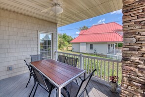 Une terrasse couverte avec une table et des chaises en bois, un mur en pierre et une vue sur une maison au toit rouge.