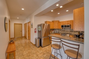 A kitchen with wooden cabinets, a stainless steel refrigerator, a microwave, and a granite countertop. - Hilltop Escape - Enjoy Lake Superior Views with City Amenities (Bayfield)