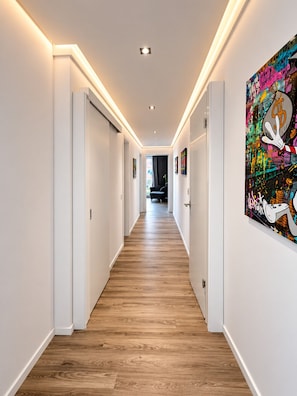 Passadís amb terra de fusta, parets blanques i una obra d'art efitàcia amb grafitis a la paret dreta.