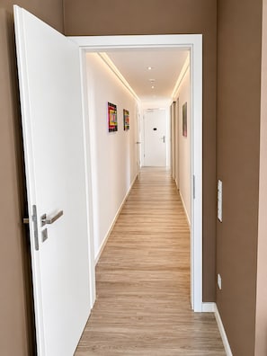 Passadís amb sòl de fusta, parets blanques i una porta amb nansa platejada.
