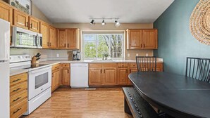 Eine Küche mit Holzausstattung, einer Mikrowelle, einem Backofen, einem Geschirrspüler und einem Esstisch mit Stühlen.