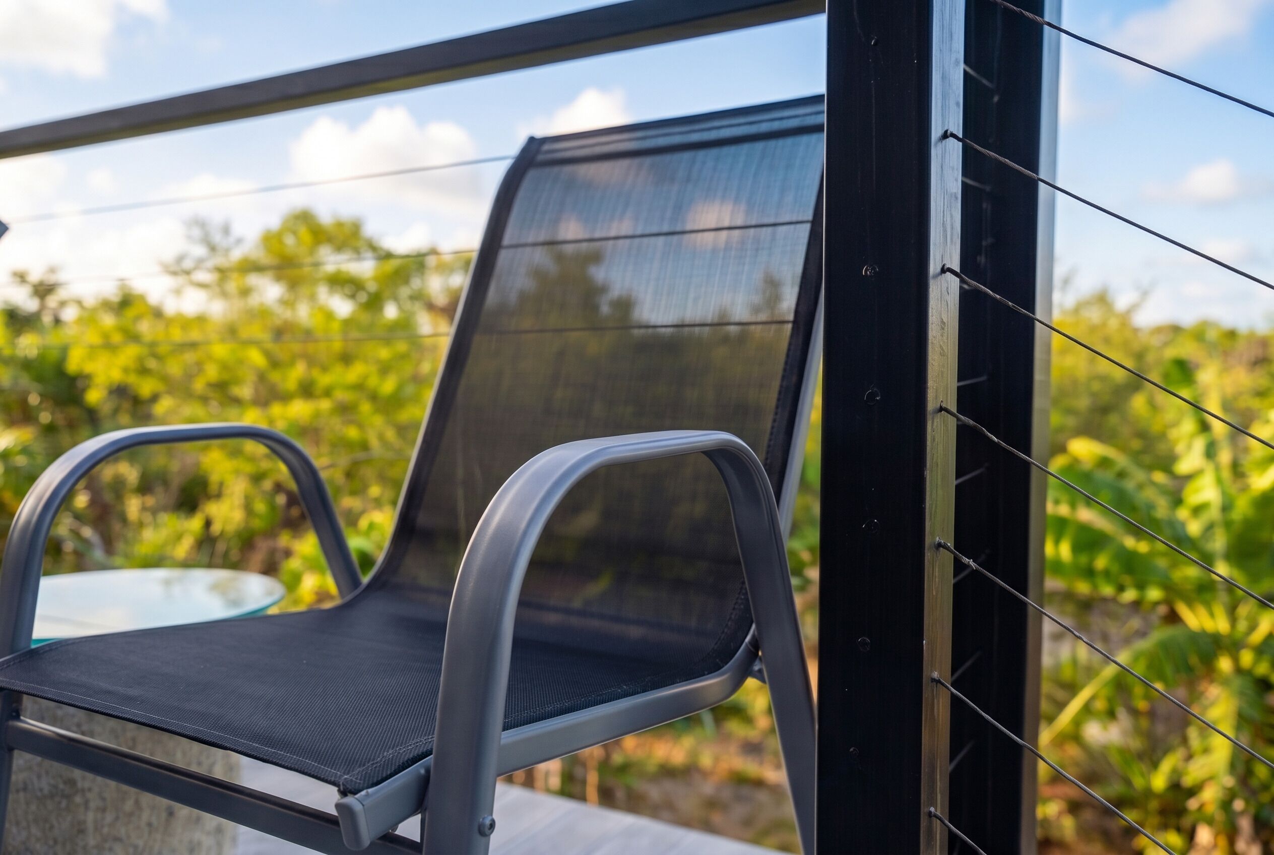 A chair with a mesh backrest and armrests, positioned near a glass table on an outdoor patio.