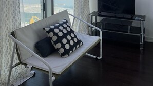 Ett modernt vardagsrum med en soffa, en tv på ett tv-bord och stora fönster med gardiner.
