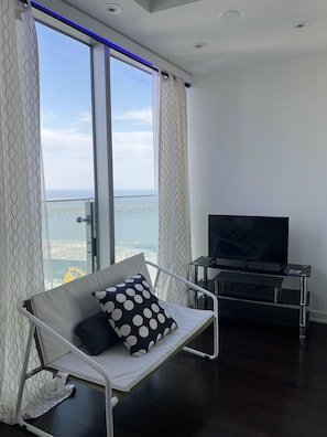 A modern living room with a sofa, a TV on a stand, and large windows with curtains. - The Velaire Toronto (Toronto)