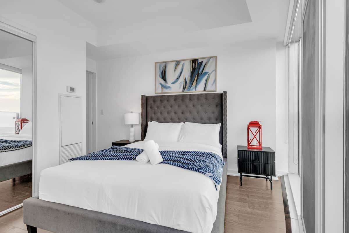 Una habitación de hotel moderna con una cama grande, un cabecero tapizado en gris, un farol rojo y un cuadro abstracto enmarcado en la pared.