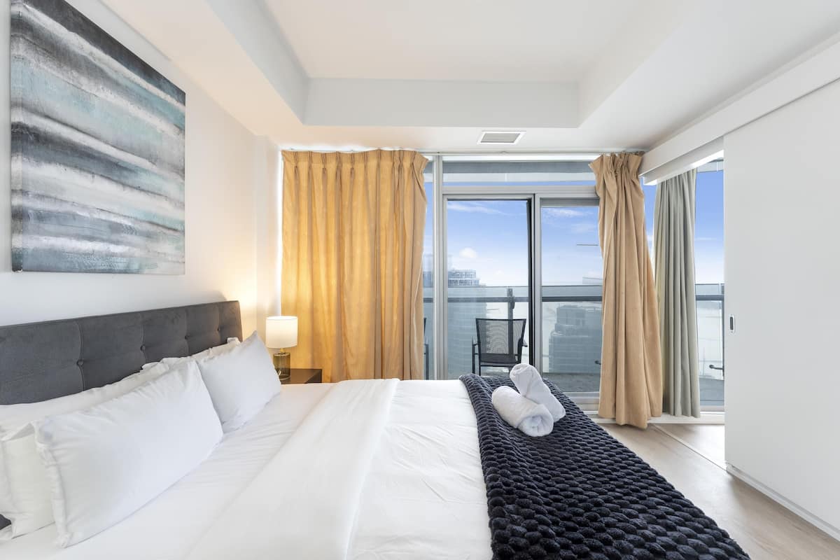Habitación de hotel con una cama grande, vistas a la ciudad y un balcón con cortinas.