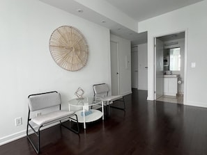A modern living room with a large wall art piece, two sofas, a coffee table, and a kitchen area visible through an open doorway. - The Velaire Toronto (Toronto)