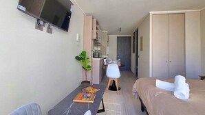 Une chambre d’hôtel comprenant un lit, un bureau avec une chaise, un téléviseur fixé au mur, une plante et une armoire.