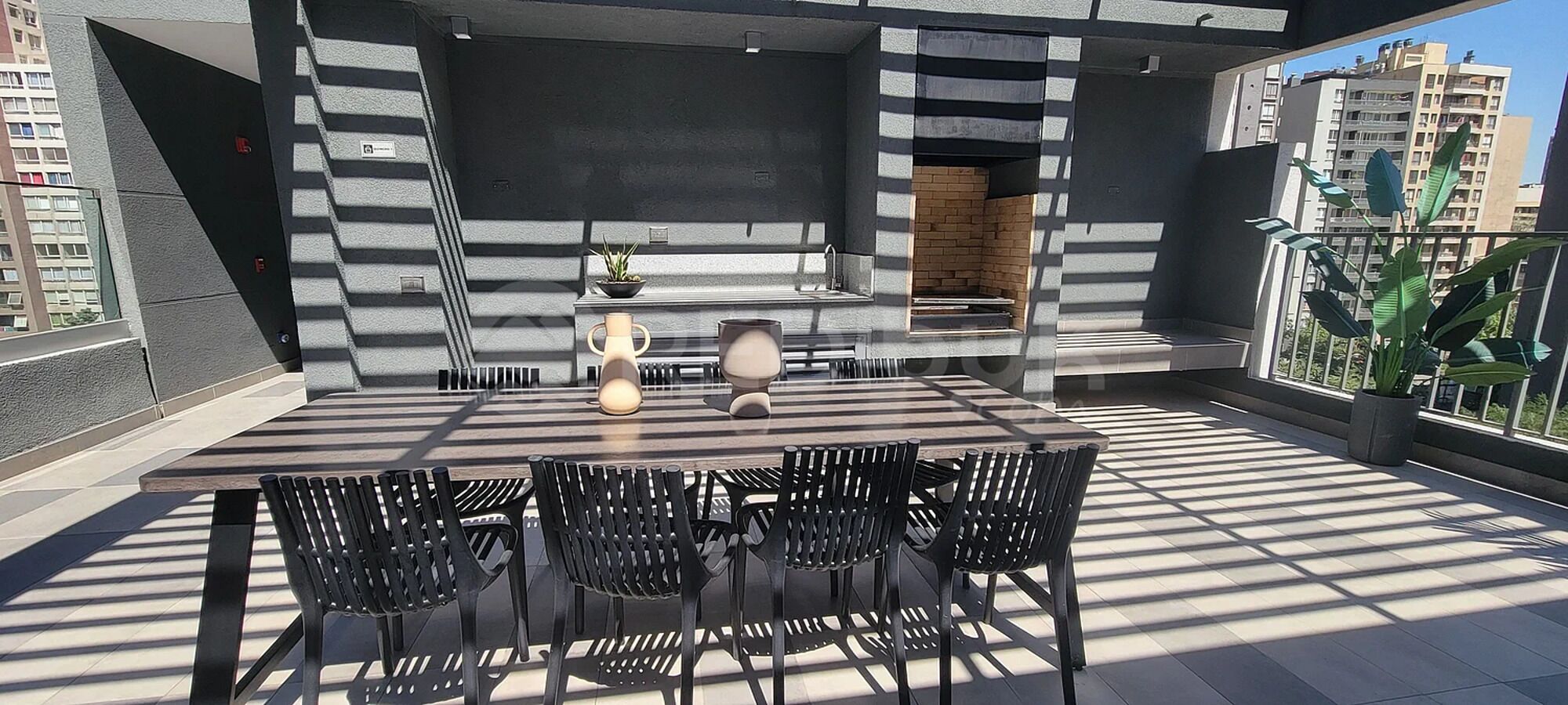 An outdoor patio with a table and chairs, a potted plant, and a brick wall.