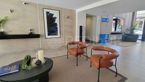 Un hall d’entrée avec un comptoir de réception, deux fauteuils à accoudoirs incurvés, un tableau abstrait encadré, une plante en pot et un panneau bleu.
