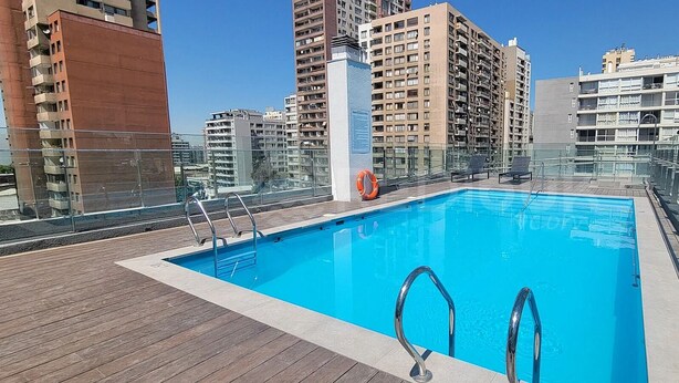 Une piscine sur le toit, entourée de bâtiments de grande hauteur et dotée de rampes en verre.