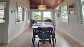 Een eetruimte met een houten plafond, grote ramen en een centrale tafel met stoelen.