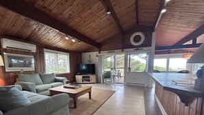 Een ruime woonkamer met houten plafond, een televisie, een bank en een salontafel.