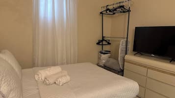 Ein Hotelzimmer mit Bett, Fernseher, Wäscheständer und Koffer.