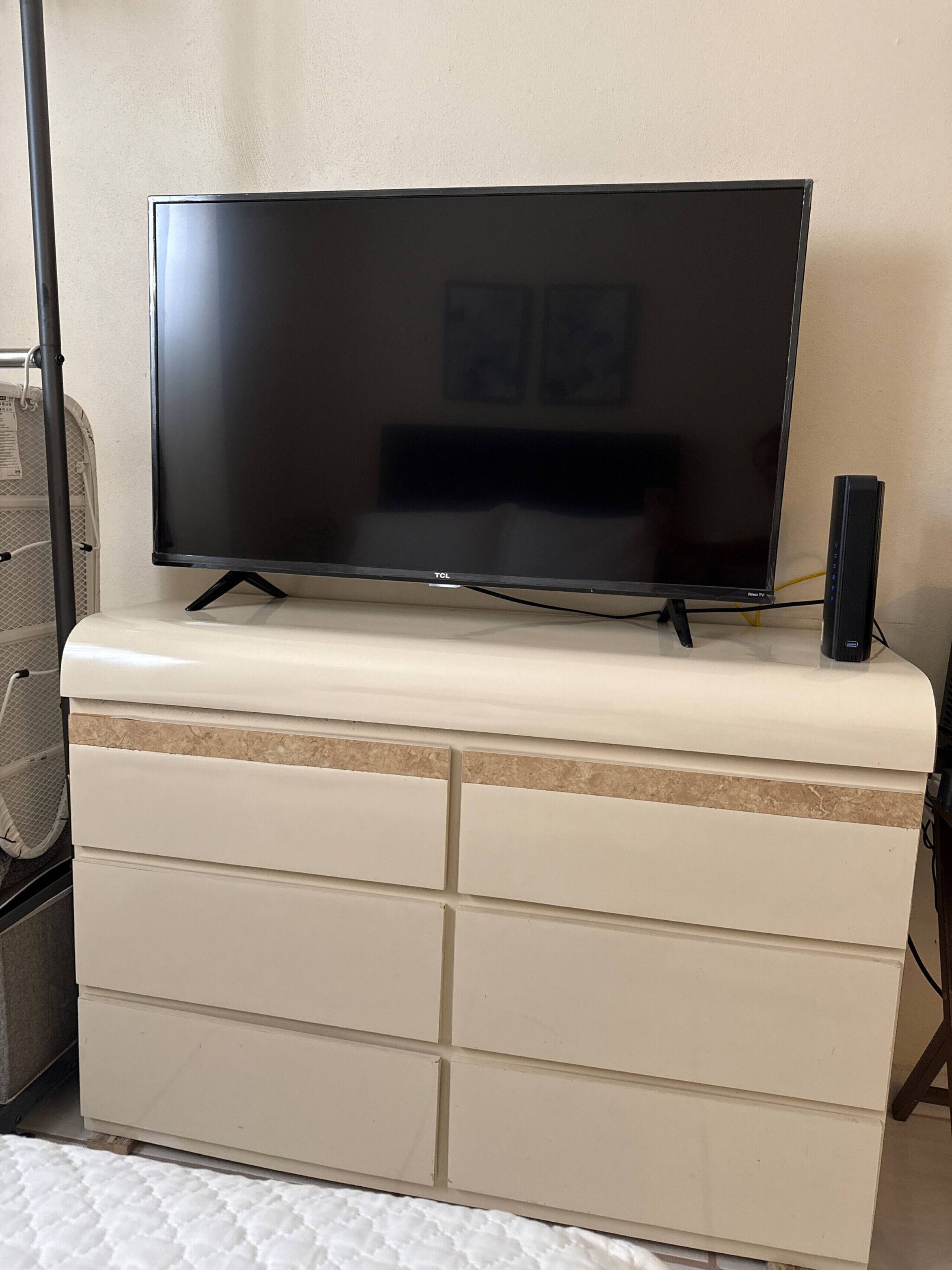 A flat-screen TV on a white dresser with drawers, a small speaker, and a power strip.
