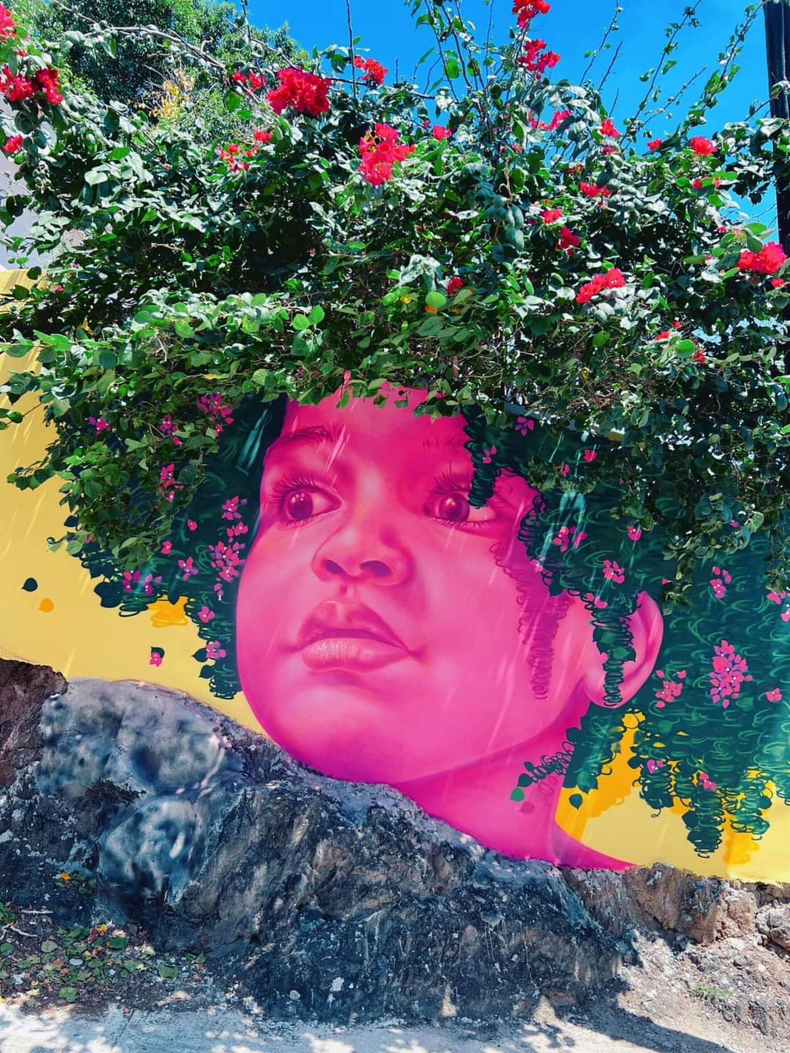 Ein Wandgemälde mit einem großen Felsen im unteren Bereich, einer gelben Wand und roten Blumen.