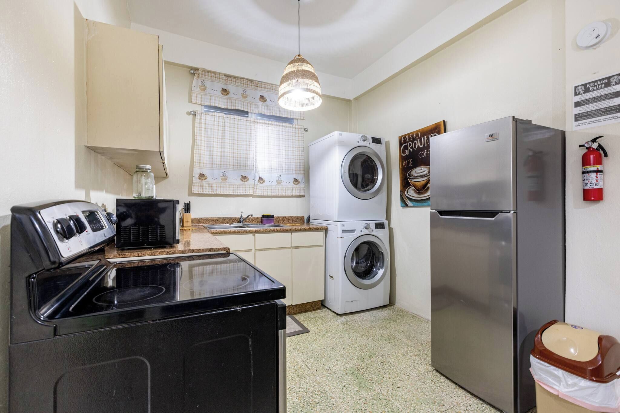 A compact kitchen with a stove, washing machine, refrigerator, and a hanging light fixture.