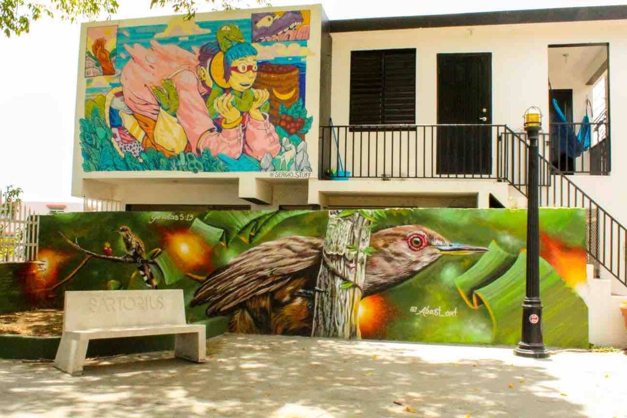 A building with a mural, a bench, and a bird sculpture.