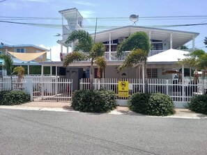 A two-story building with a white exterior, a balcony, and a fenced entrance.