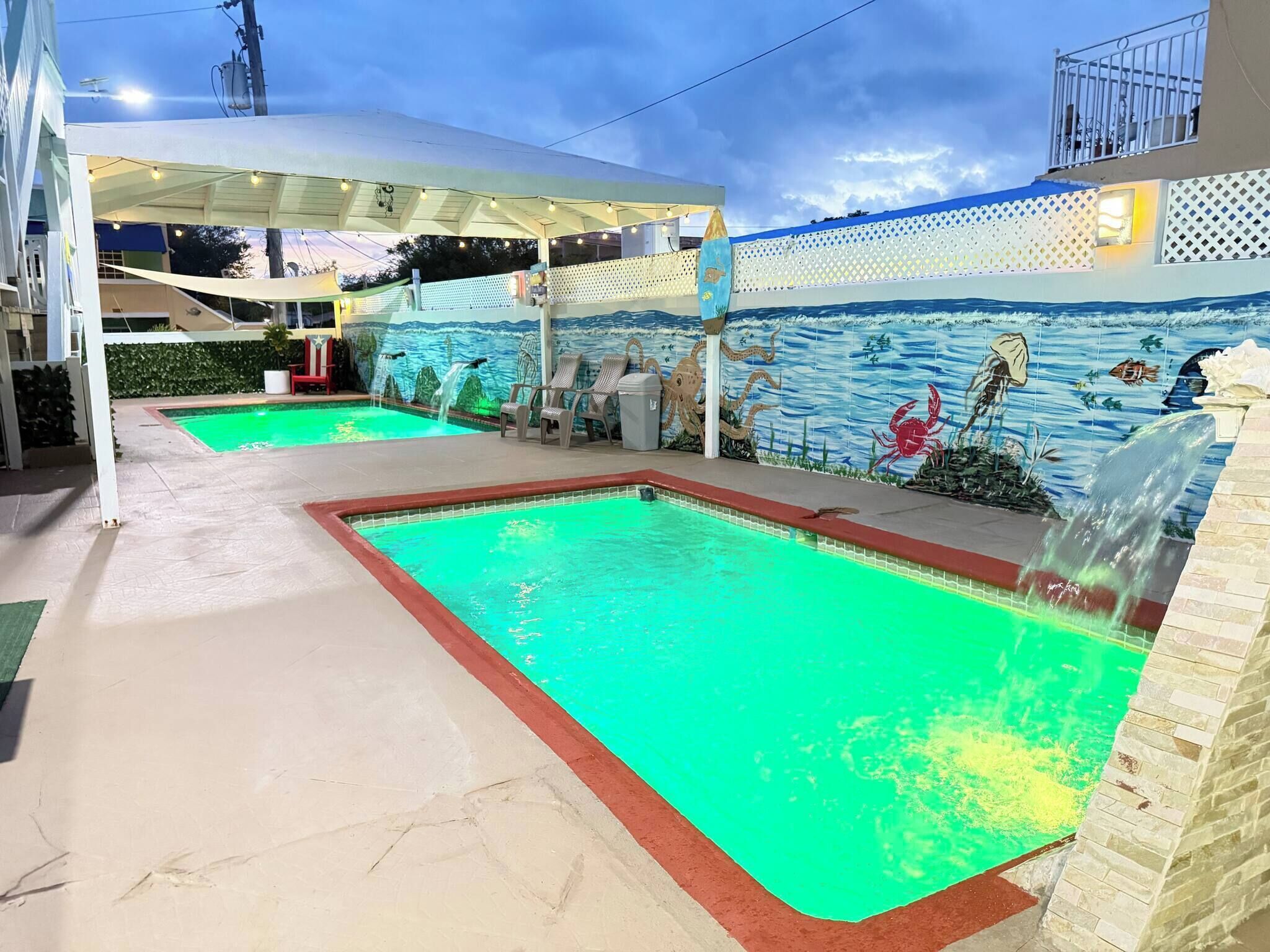 Une piscine ornée d’une fresque murale, un espace de repos abrité et un élément décoratif aquatique.