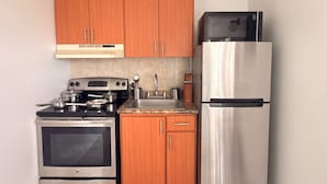 A compact kitchen with wooden cabinets, a stainless steel refrigerator, an oven, and a microwave.