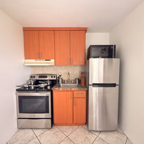 Una cocina compacta con armarios de madera, un refrigerador de acero inoxidable, un horno y un microondas.