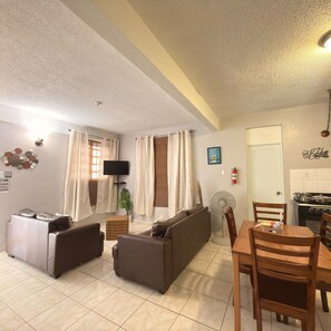 Una sala de estar con sofá, una mesa de comedor y una zona de cocina con estufa.