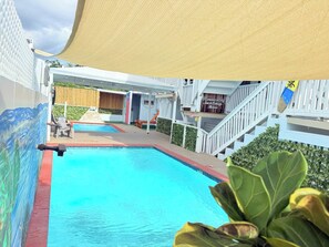 Une piscine avec une terrasse en bois, un espace salon couvert et un escalier menant à un niveau supérieur.