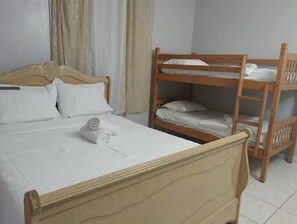 Un lit simple avec une tête de lit en bois, un lit superposé en bois et une fenêtre avec des rideaux.