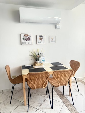 Un comedor con una mesa, sillas de mimbre, una planta en maceta y arte en la pared que representa bebidas de café.