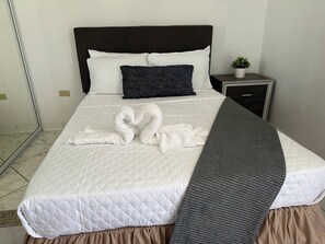 Ein ordentlich bezogenes Bett mit einer gesteppten weißen Daunendecke, einem dunklen Kopfteil und einem einzelnen dunklen Kopfkissen.