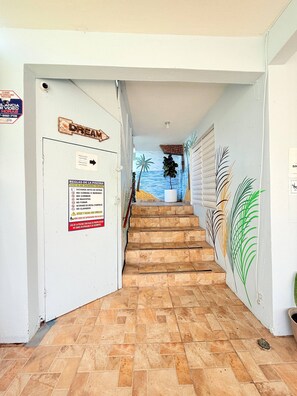 Un pasillo con un letrero que indica la zona de la piscina, una escalera y un mural con palmeras.