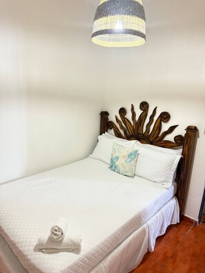 A neatly made bed with a white quilt, a decorative headboard, and a hanging light fixture. - Private balcony, near Playa Santa (Guanica)