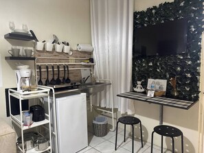 A compact kitchen with a coffee maker, utensils, and a small refrigerator.
