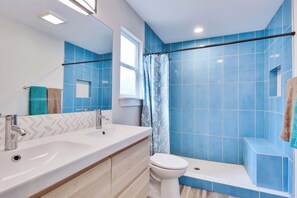 Ein Badezimmer mit einem großen Spiegel, zwei Waschbecken, einer Toilette und einem Duschbereich mit blauen Fliesen.